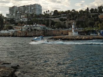 Sailboats in sea by buildings against sky