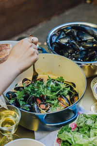 Woman's hand using fork to pick steamed mussels out of pot at dinner table