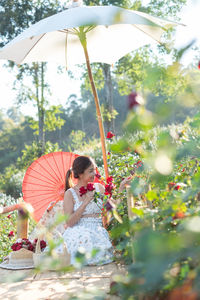 Young asian woman wearing a white dress poses with a rose in rose garden, chiang mai thailand