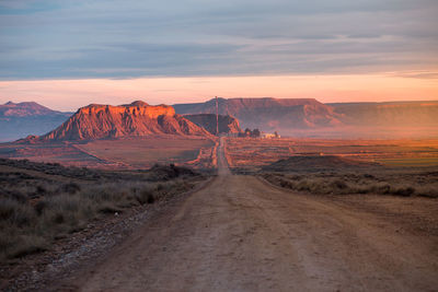 Dirt road amidst landscape against sky during sunset