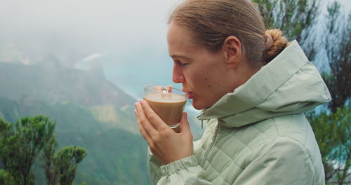 Girl enjoying cup of cappuccino in the forest at foggy morning. portrait of woman drinking coffee.