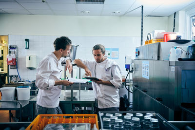 Male chefs with digital tablet and documents in kitchen