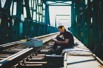 Full length of engineer reading book while sitting on railroad track