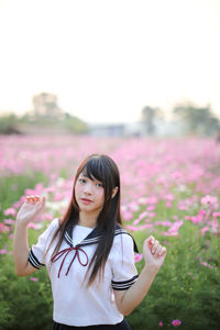 Portrait of beautiful woman standing by pink flower on field