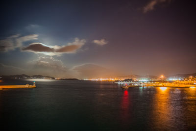 Night view of athens piraeus harbor with moon partially hidden by clouds, greece