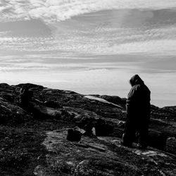 Rear view of man standing on rock by sea against sky