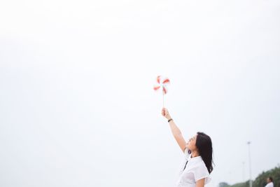 Low angle view of woman holding balloons against clear sky
