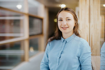 Portrait of happy young businesswoman standing at office corridor