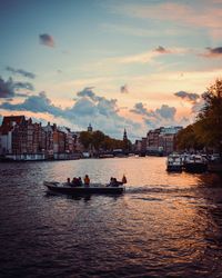 Scenic view of river by buildings against sky during sunset