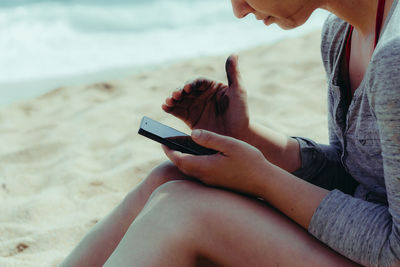 Midsection of woman using mobile phone at beach