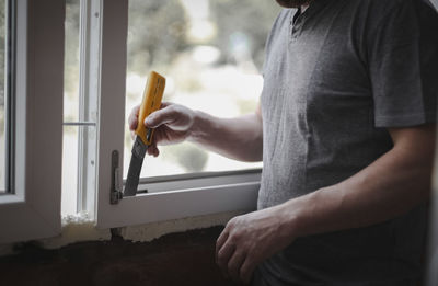 Caucasian man cleans a window frame with a construction knife.