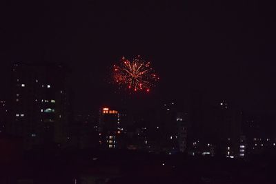 Firework display in city against sky at night