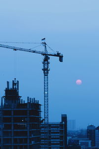 Low angle view of crane and buildings against blue sky