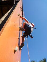 Low angle view of person climbing wall against sky