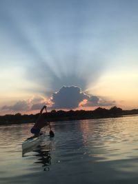 Man rowing boat in lake against sky during sunset