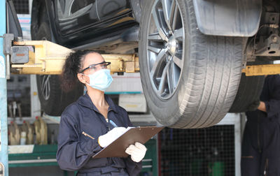 Female worker wearing mask examining car in garage