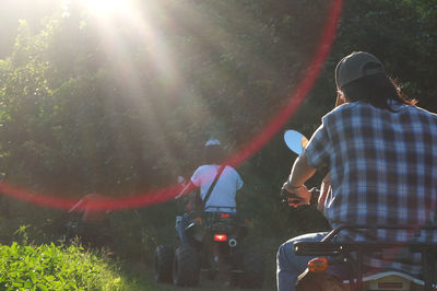 Rear view of people riding quadbikes in forest during sunny day
