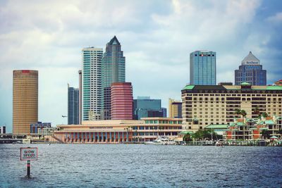 Modern buildings by river against sky in city