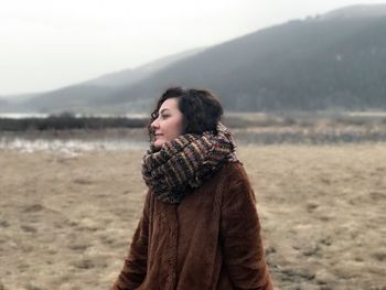 Woman in warm clothing standing on field against sky