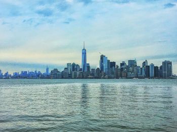 View of city at waterfront against cloudy sky