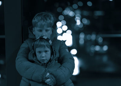 Portrait of boy with brother standing against illuminated lights at night