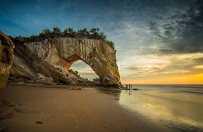 Rock formation on beach against sky during sunset