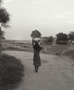 Rear view of woman walking on field against sky