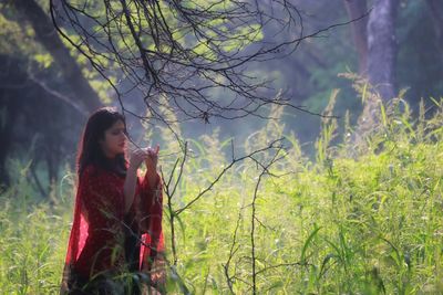 Woman standing by tree on field in forest