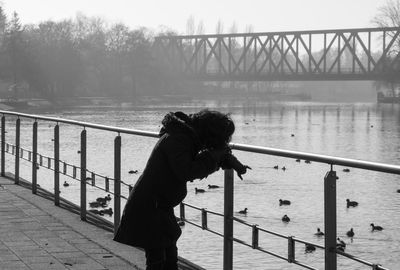 Side view of woman photographing while standing by river on footpath