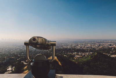 Close-up of coin-operated binoculars on retaining wall over cityscape at griffith point observatory