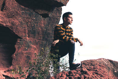 Young man looking away while sitting on rock
