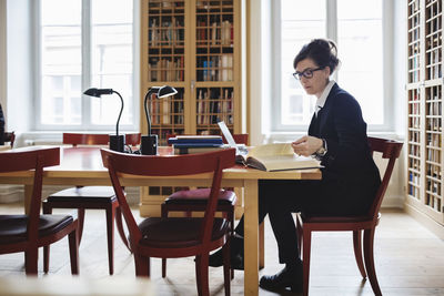 Side view of female professional reading book at table in law library