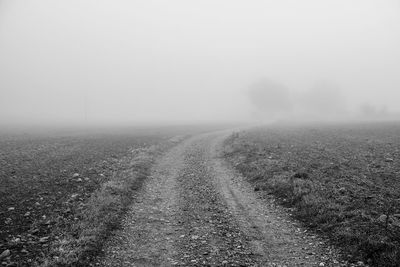 Dirt road on field against sky during foggy weather