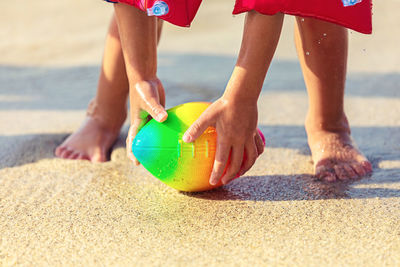 Low section of person picking ball at beach