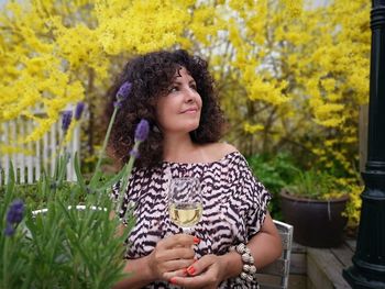 Woman with wineglass looking away while standing in yard