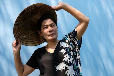 Mature woman wearing asian style conical hat against wall