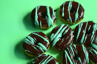 Donuts with chocolate frosting and stripes of green frosting on green paper