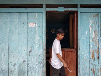 Side view of man standing against door of building