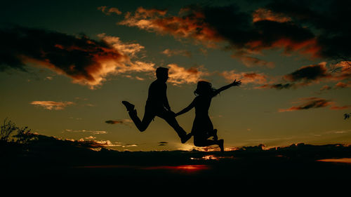 Silhouette man jumping against orange sky