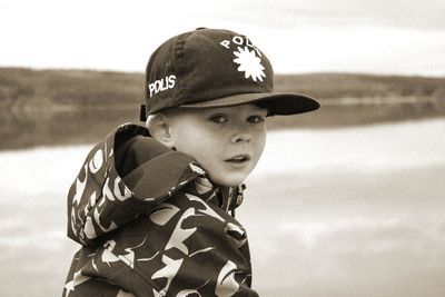 Close-up portrait of boy wearing cap against river