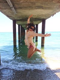 Woman jumping underneath pier over sea