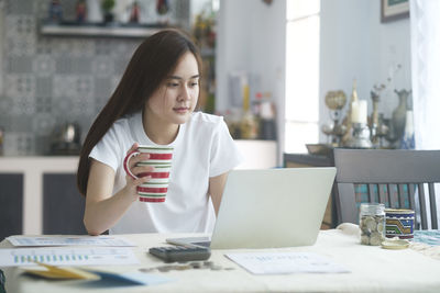 Young woman using phone while sitting on table