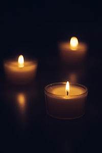 Close-up of tea light candles burning in darkroom