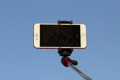 Low angle view of mobile phone on monopod against clear blue sky