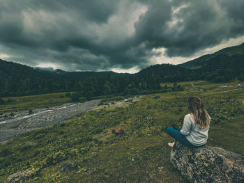 Woman sitting on mountain against sky