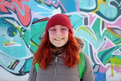 Portrait of smiling young woman standing against graffiti
