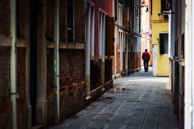 Rear view of man walking on footpath amidst buildings