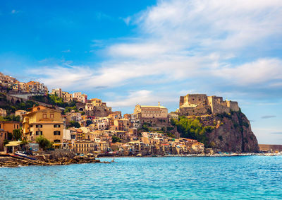 Buildings by sea against sky