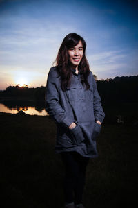 Portrait of smiling young woman standing on field against sky