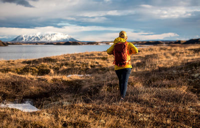 Woman walking away from camera with backpack next to lake